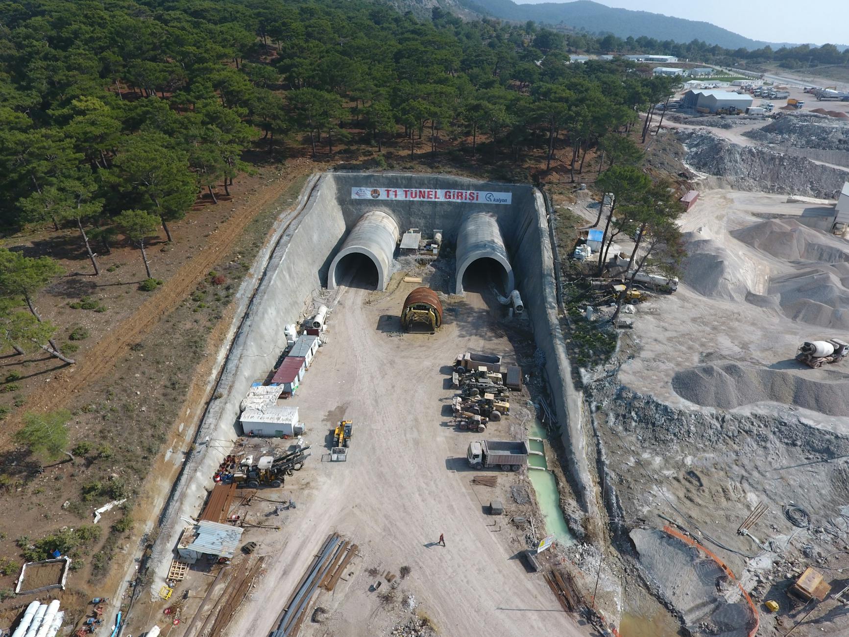 Aerial shot of Yeniçam tunnel construction site in Çanakkale, Turkey, showcasing heavy machinery and forest surroundings.