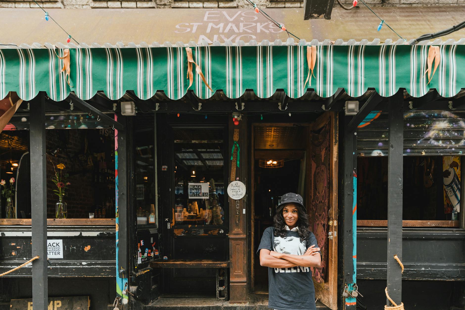Portrait of confident young black woman standing at a vibrant, colorful cafe entrance in the city.