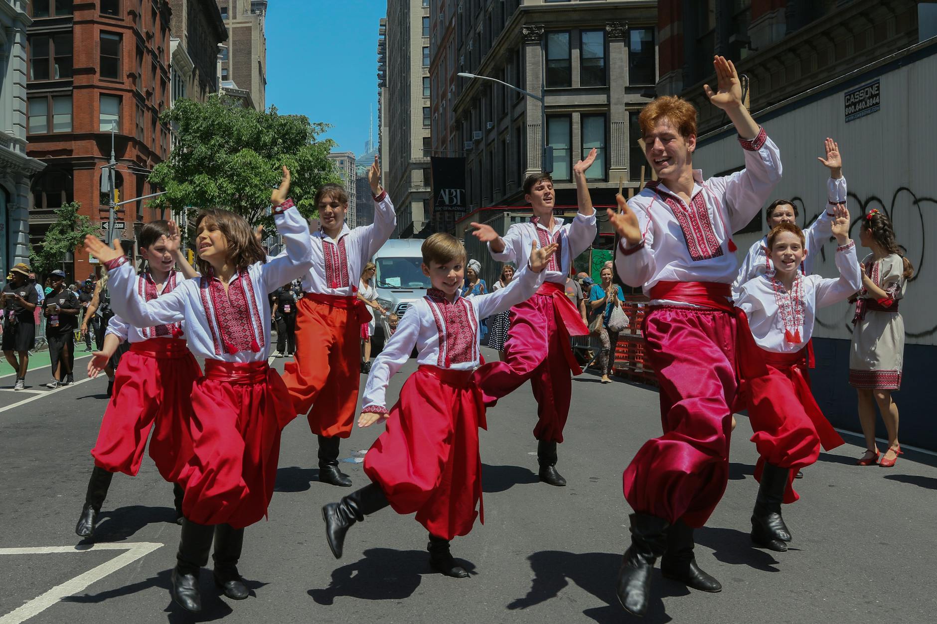 Group of dancers in traditional attire performing on a street in New York City during a summer festival.